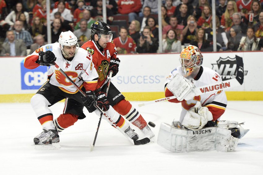 Calgary Flames goalie Joey MacDonald, right, swats the puck away as Chicago Blackhawks' Patrick Sharp, center, tries to score and Flames' Mark Giordano defends during the second period of an NHL hockey game, Friday, April 26, 2013 in Chicago.  (AP Photo/Brian Kersey)