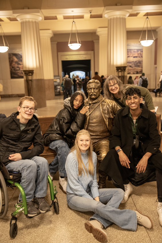Four Feather students and chaperone pose for a picture with the statue of Theodore Roosevelt who instigated the creation of the museum.